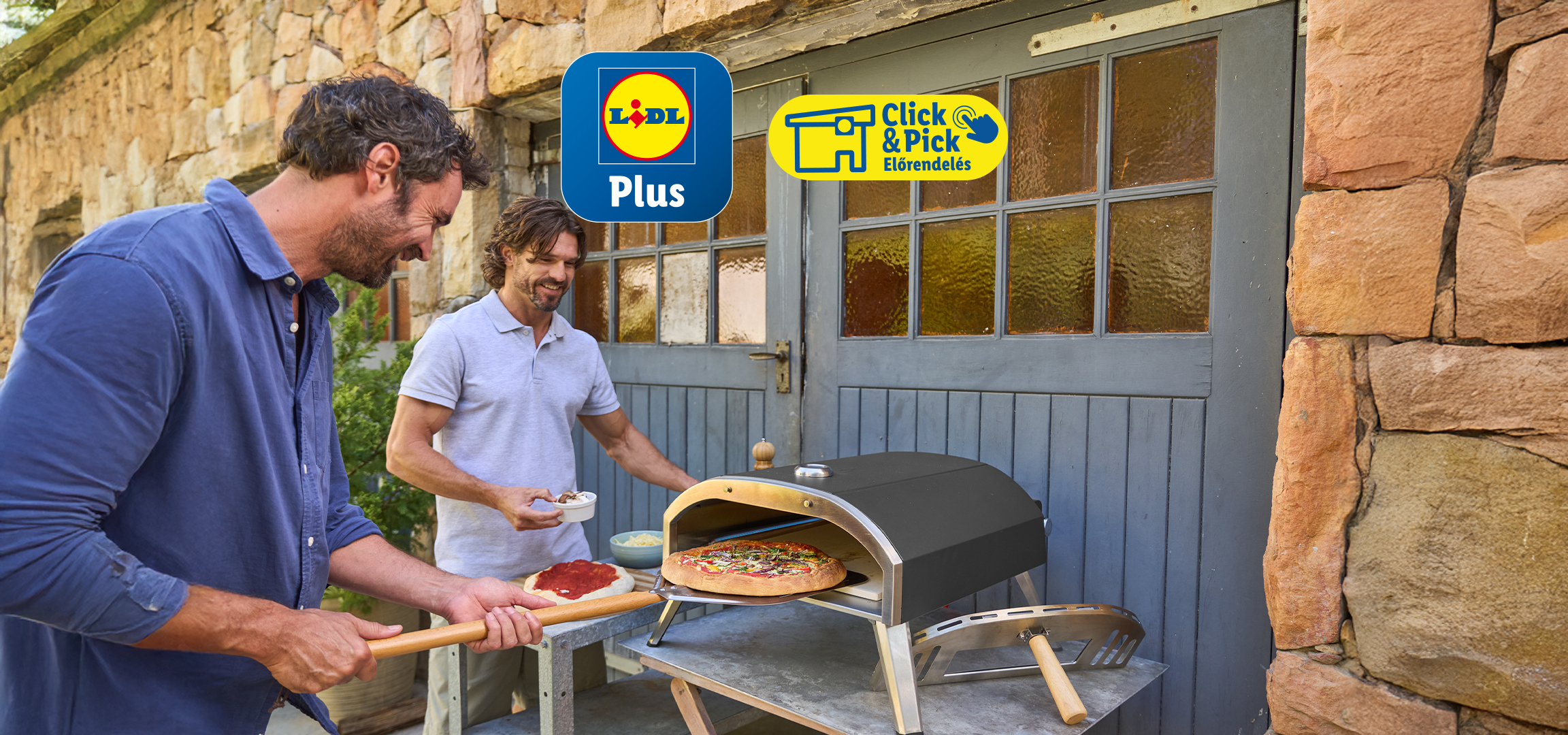 Két férfi pizzát süt egy kültéri pizzasütőben, az egyik éppen kiveszi a kész pizzát.