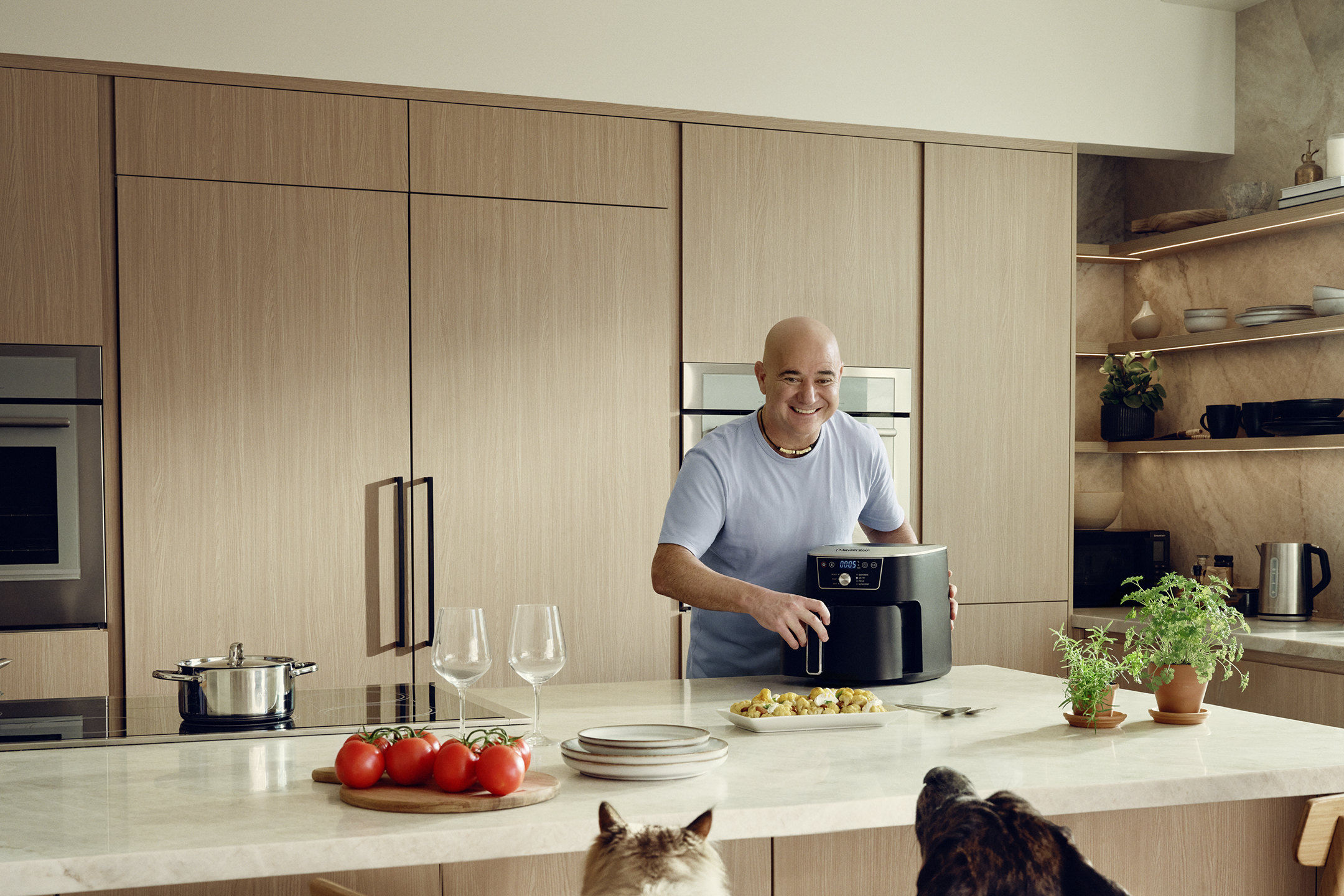 Andre Agassi a konyhában egy forrólevegős fritőzzel ételt készít, miközben kutyák figyelik.