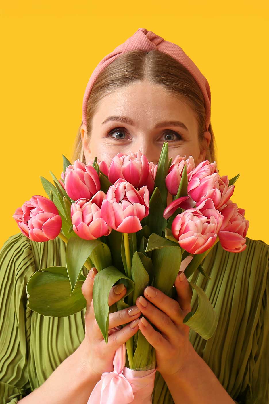 Nő rózsaszín tulipáncsokorral, sárga háttér előtt.