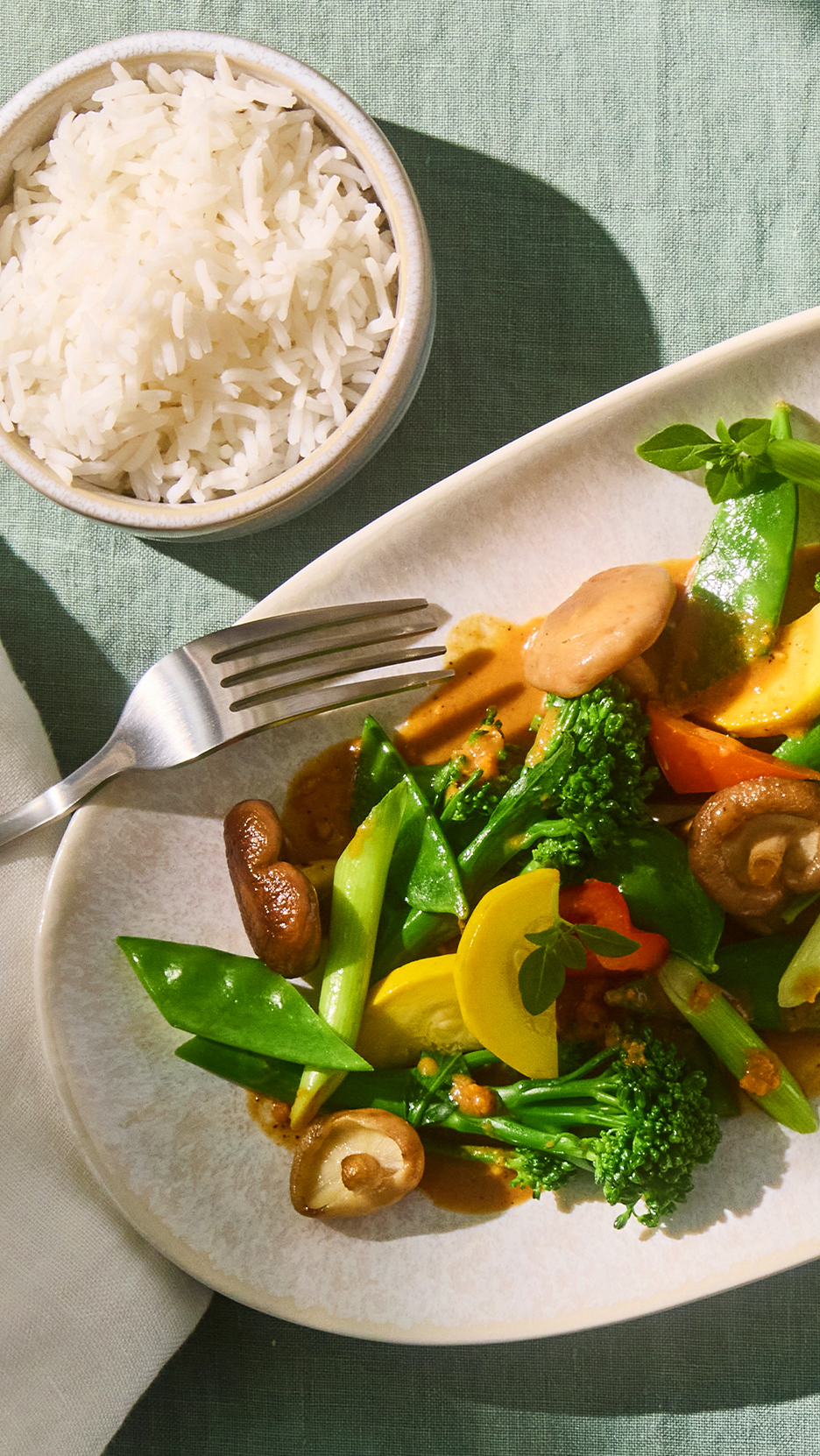 Zöldséges curry rizzsel és villával egy világos tányéron, zöld terítőn.