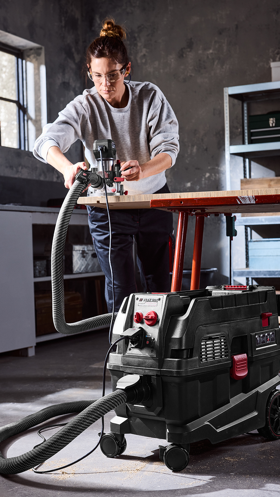 Nő dolgozik egy asztali marógéppel, amelyhez porszívó van csatlakoztatva.