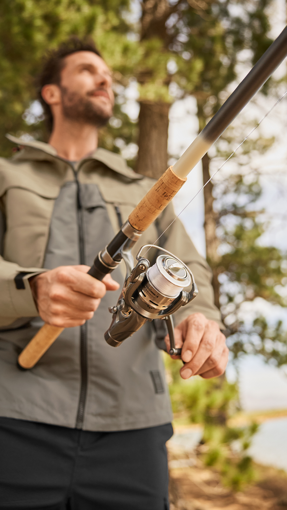 Férfi horgászbotot és orsót tartva, horgászruhában, a szabadban.