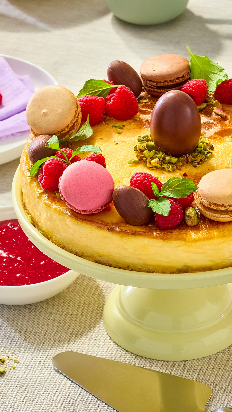 Sajttorta macaronokkal, málnával és csokoládétojásokkal díszítve, tortatálon.