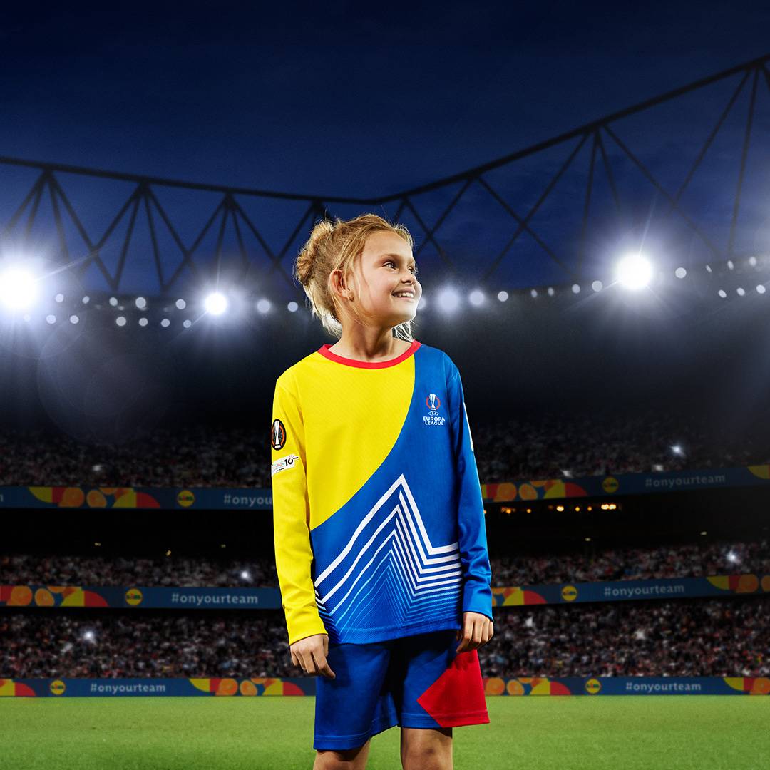 Lány UEFA Europa League mezt és rövidnadrágot visel egy futballstadionban.