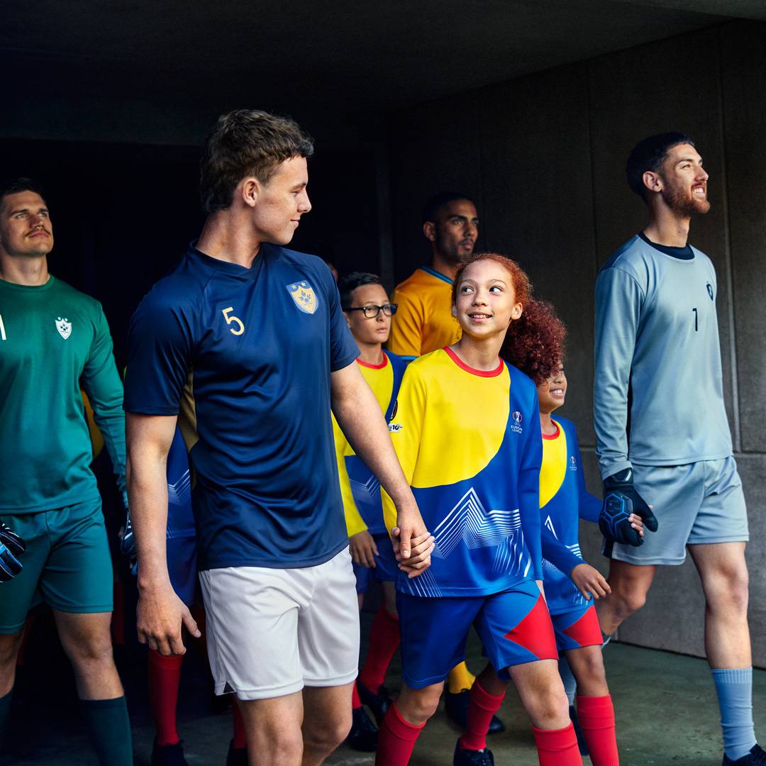 Felnőtt és gyermek focisták vonulnak a pályára, sportruházatban.