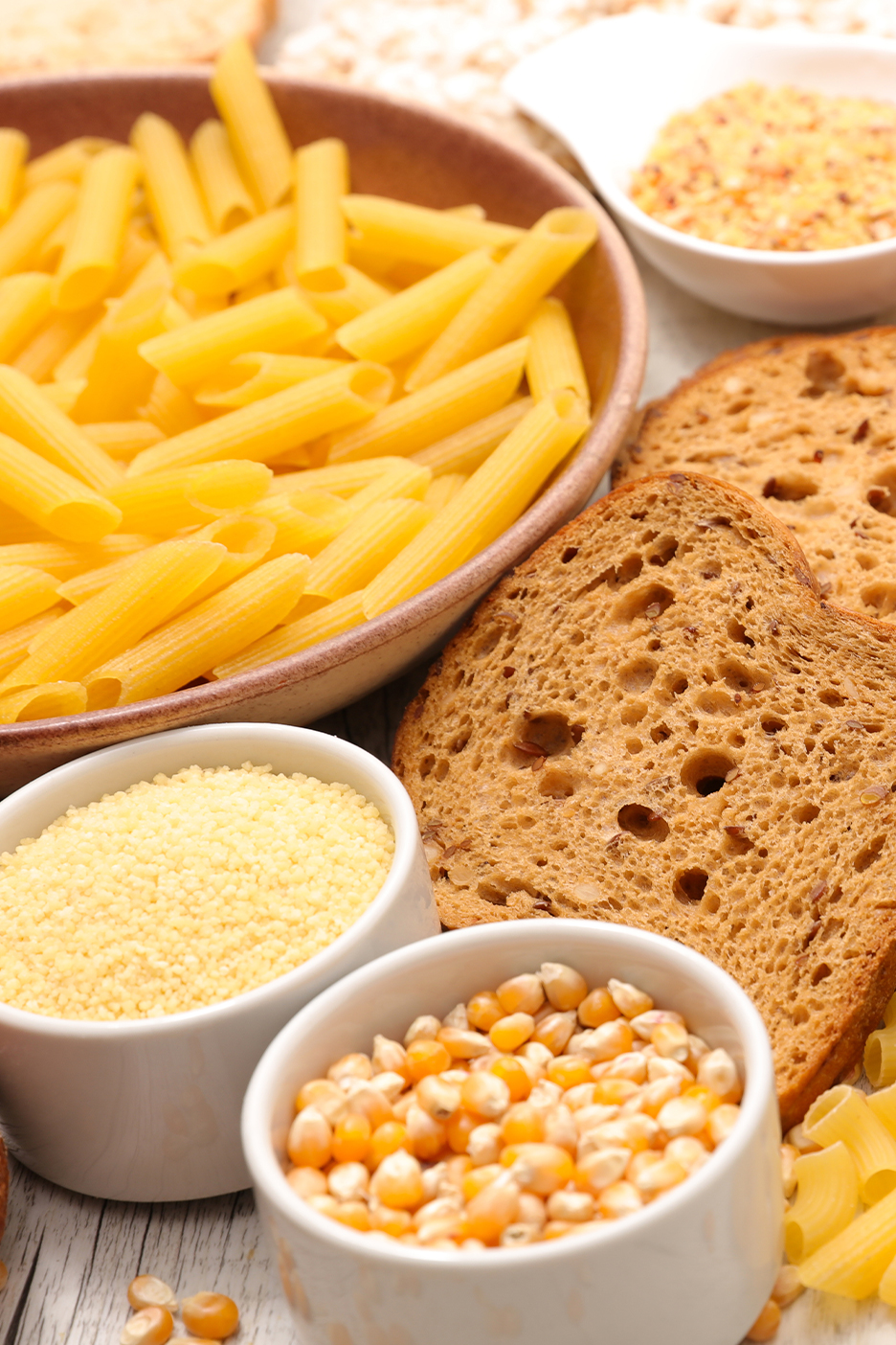 Különböző gabonafélék és tésztafélék, köztük penne, kenyérszeletek, kuszkusz és kukoricaszemek.