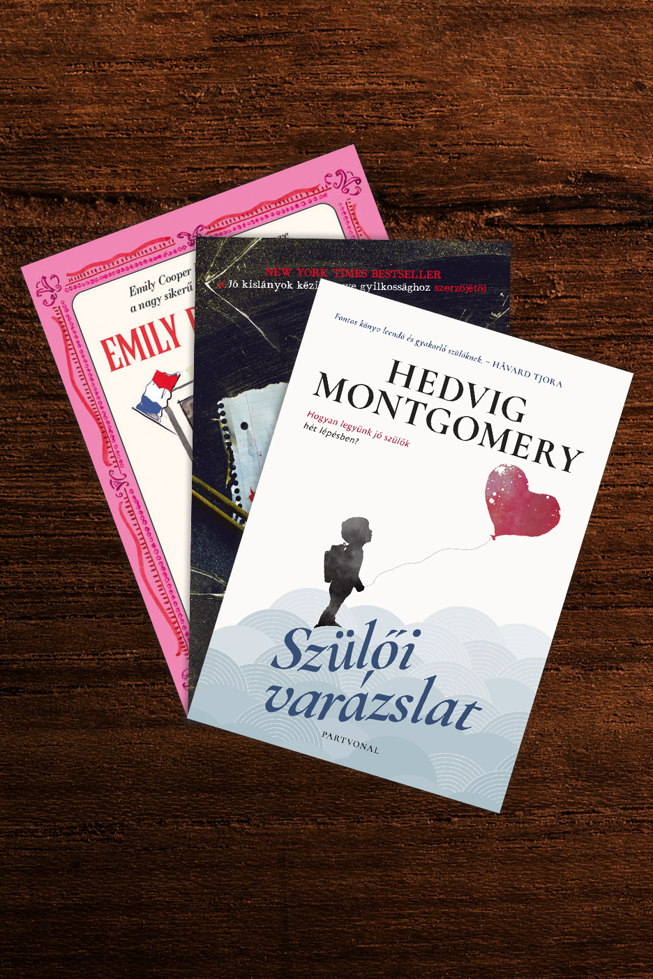 Három könyv, köztük egy szülői útmutató és egy regény, fa asztalon.