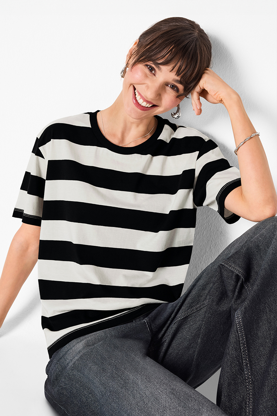 Női fekete-fehér csíkos póló és sötét farmernadrág, mosolygó nőn.