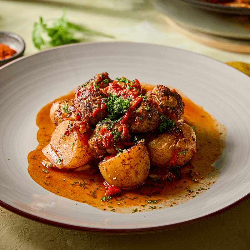 Húsgombócok paradicsomszósszal és burgonyával, petrezselyemmel díszítve egy tányéron.