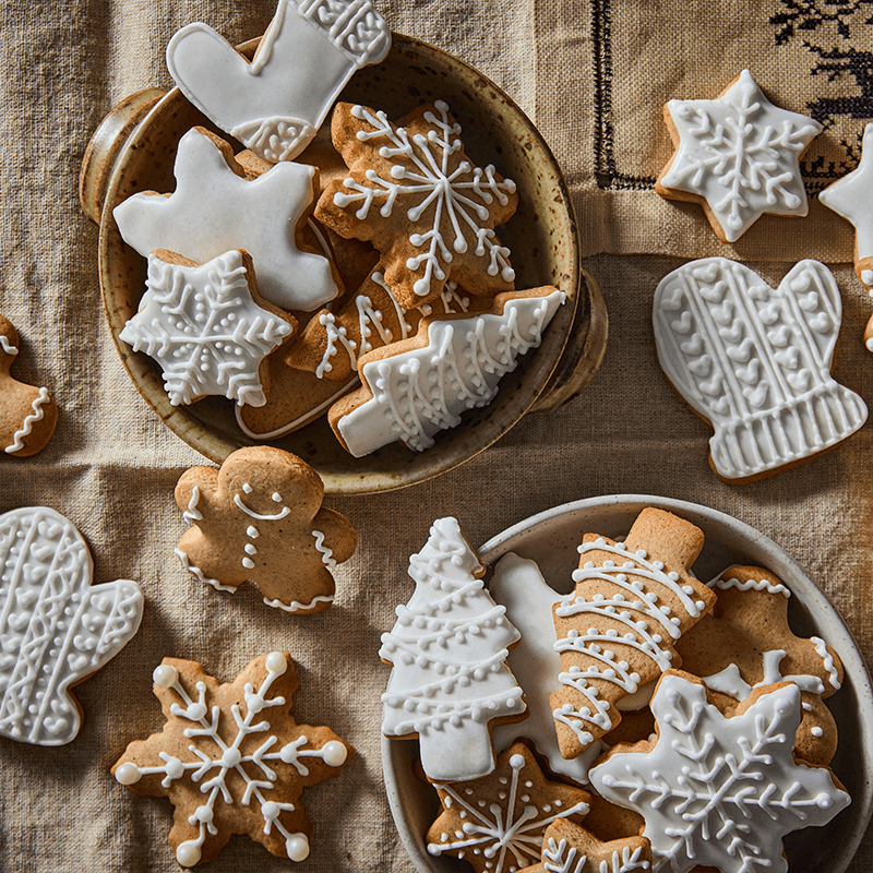 Mézeskalács karácsonyi sütik, fehér cukormázzal díszítve, tálakban és asztalon.
