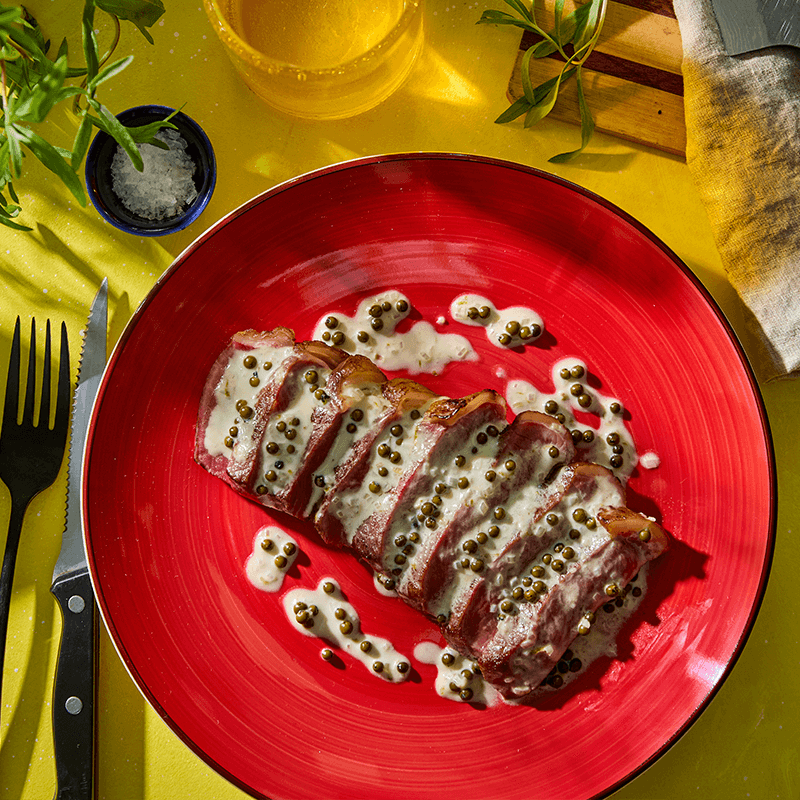 Szeletelt hús zöldborsmártással, piros tányéron, evőeszközökkel és fűszerekkel.