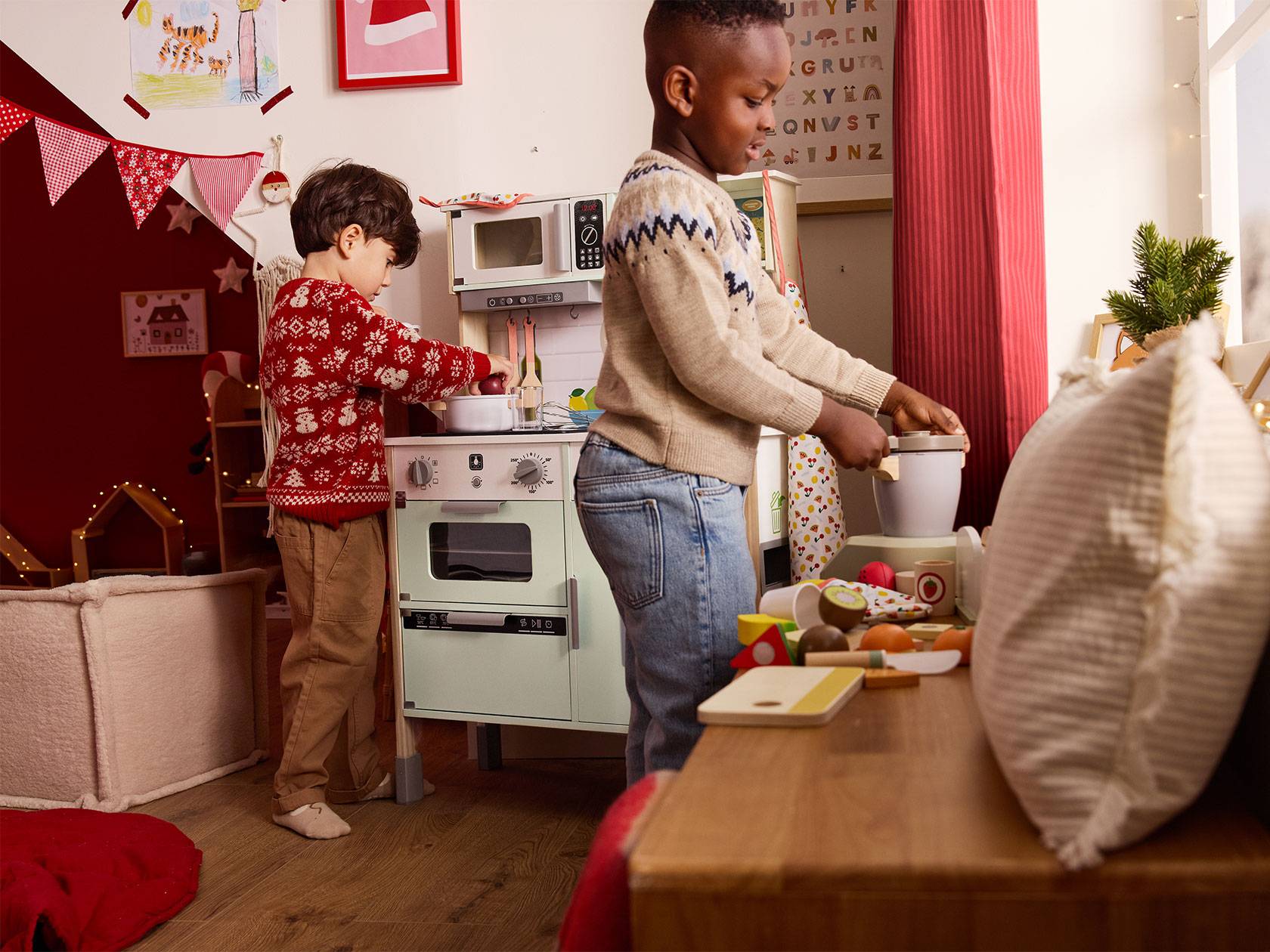 Két gyermek játszik egy fából készült játékkonyhával, karácsonyi dekorációkkal.