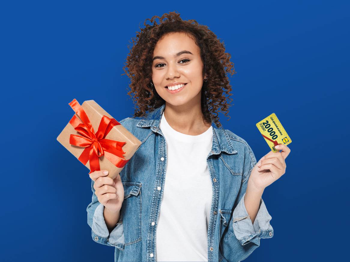 Egy mosolygós fiatal nő Lidl ajándékkártyát és ajándékcsomagot tart a kezében.